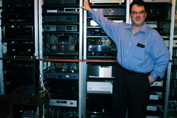 Dave Lalin, owner of Audio Intellect, standing in front of tall racks of audio equipment