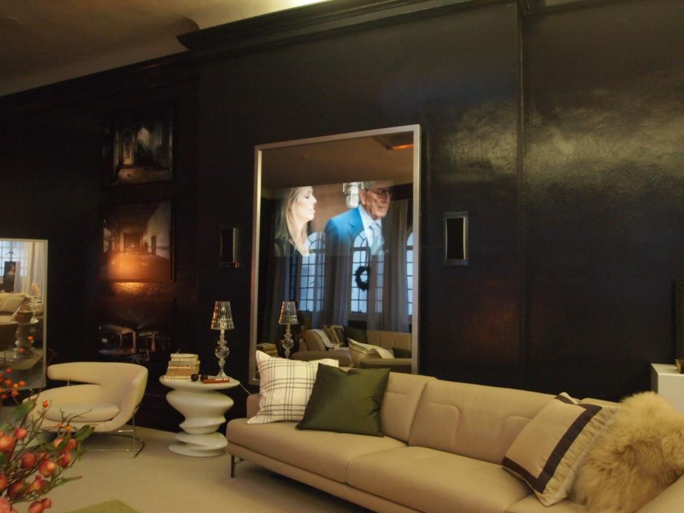 A dark lounge with a television hidden behind a mirror, showing a picture through the glass